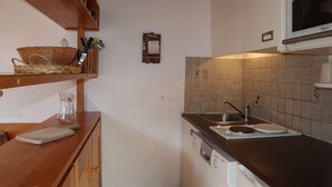 Una cocina con estantes de madera, microondas, lavaplatos y fregadero.