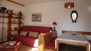 Un salón acogedor con un sofá rojo, estanterías de madera, una mesita y una lámpara colgante.