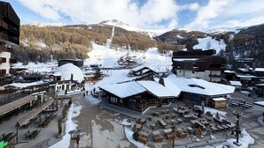 A ski resort with outdoor seating areas, a mountain view, and a snow-covered landscape.