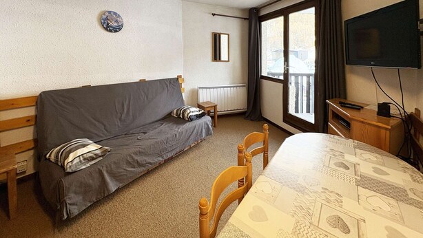 A room with a sofa, a table, a chair, a television, and a window with curtains.