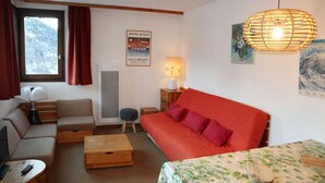 A cozy room with a sofa, a bed, a wooden coffee table, a lamp, and a window with curtains. - APARTMENT N° 407 LE CAIRN (LES ORRES 1650)