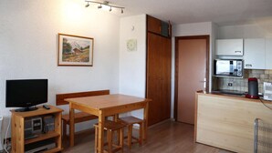 A compact living space with a wooden dining table, a television, a kitchenette, and a door leading to another room. - COEUR STATION LES ORRES - Res. CAIRN - Studio 4 pers (LES ORRES 1650)