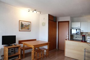A compact living space with a wooden dining table, a television, a kitchenette, and a door leading to another room. - COEUR STATION LES ORRES - Res. CAIRN - Studio 4 pers (LES ORRES 1650)