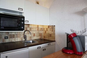 A kitchen with a built-in microwave, a sink, and a red coffee maker on the countertop. - COEUR STATION LES ORRES - Res. CAIRN - Studio 4 pers (LES ORRES 1650)