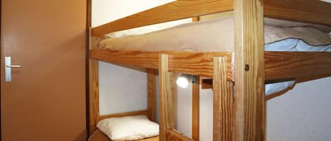 A bunk bed with a wooden frame, a door, and a light fixture on the wall.