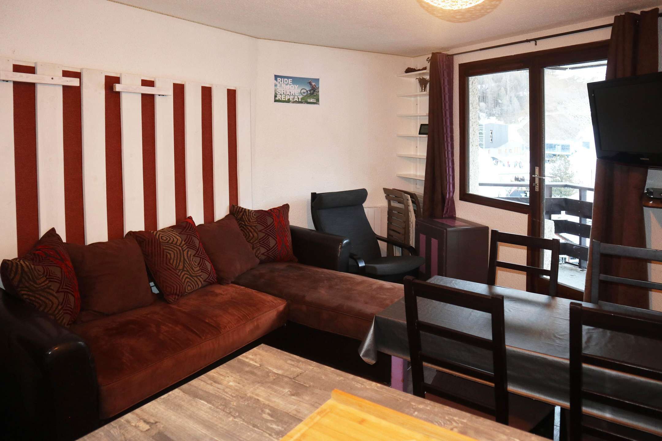 A living room with a brown sofa, a wooden coffee table, a black armchair, and a dining table with chairs.