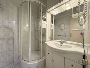 Un baño moderno con ducha envuelta en vidrio, un lavabo blanco y un espejo grande con iluminación.