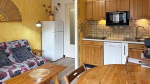 Een knus woongedeelte met een kitchenette, een eethoek en een bank met patroon kussens.