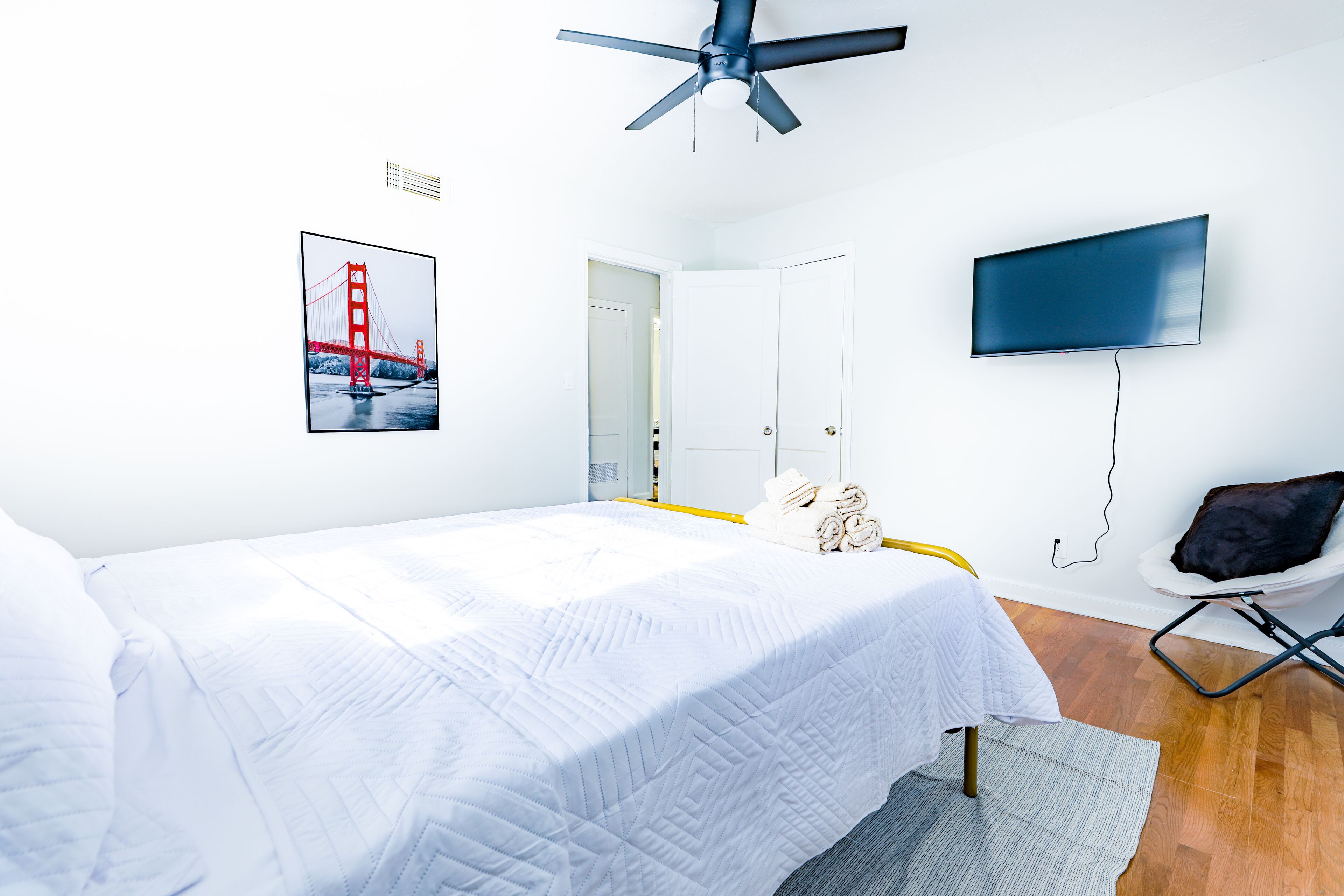A bedroom with a bed, a ceiling fan, a TV, and a door.
