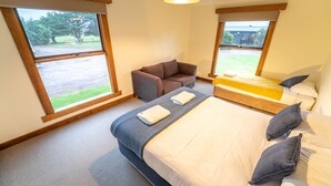 A bedroom with a large bed, a sofa, and two windows with a view of the outdoors. - Farm House Accommodation Northern end of the Bay of Fires 5 mins from Mt Willian (Musselroe Bay)
