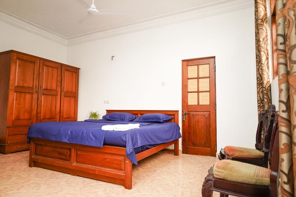 A bedroom with a wooden bed, a wardrobe, a door, and a chair. - The Anam Hostel (Colombo)