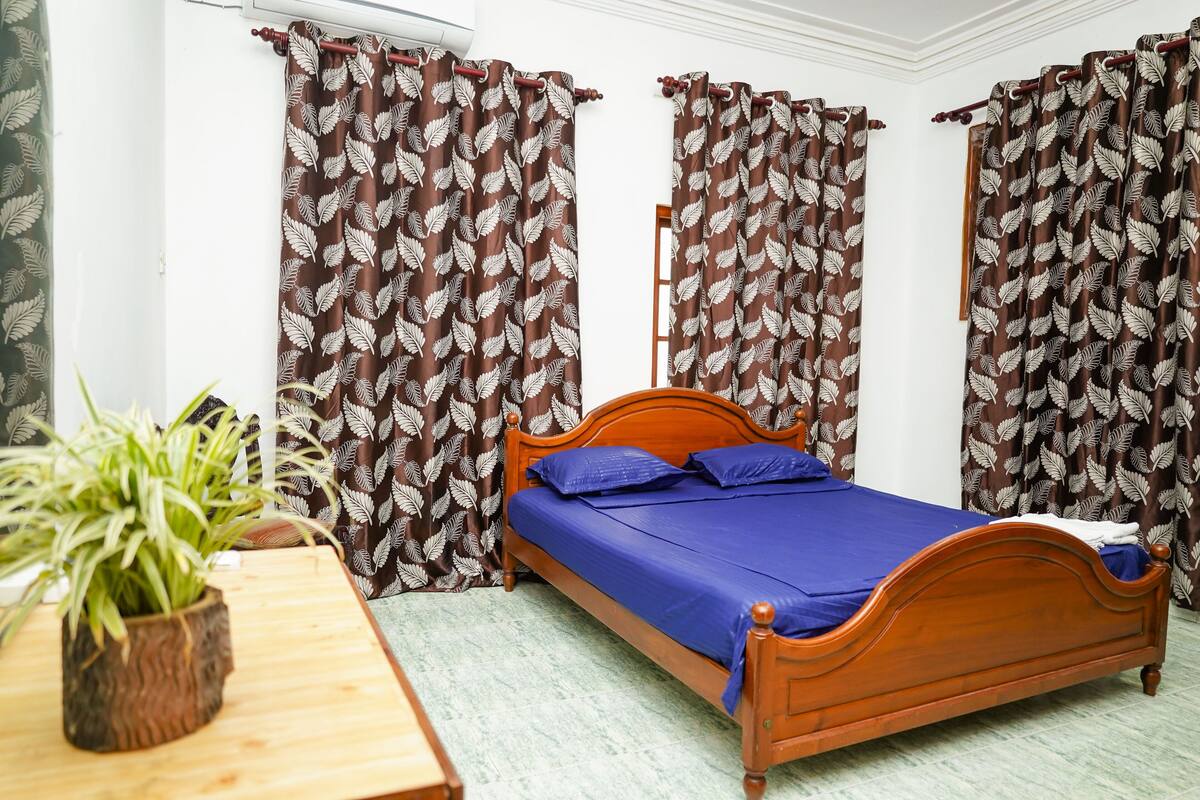 Un dormitorio con cama de madera, ropa de cama azul y cortinas estampadas.