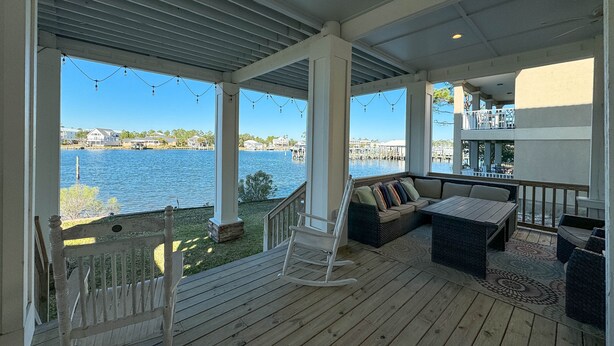 A covered outdoor deck with a rocking chair, a sofa, and a table. - Large Private Home Sleeping 16 On Cotton Bayou (Orange Beach)