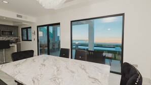 Un espace repas moderne avec une table en marbre et des chaises noires, de grandes portes vitrées donnant sur la piscine.