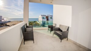Un balcon agrémenté de meubles en osier, une vue dégagée sur la mer et, en arrière-plan, un bâtiment moderne.
