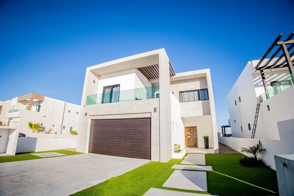 A modern two-story house with a garage, a well-maintained lawn, and a clear blue sky. - Pelican Place By FMI Rentals (Puerto Peñasco)