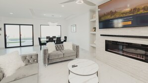 Un salon moderne avec un canapé gris, des coussins blancs et moelleux, une table basse ronde et un téléviseur à écran plat fixé au mur.