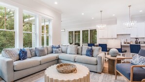 A modern living room with a sectional sofa, a round coffee table, and a dining area with a small table and chairs. - Newly built 6 bedroom home located at the end of a cul-de-sac for privacy. Large screened in porch (Bald Head Island)