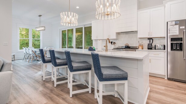 A modern kitchen with white cabinetry, a central island with bar stools, pendant lighting, and a stainless steel refrigerator. - Newly built 6 bedroom home located at the end of a cul-de-sac for privacy. Large screened in porch (Bald Head Island)