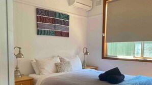 A bedroom with a bed, two bedside tables, a wall art piece, a window with blinds, and a wooden floor. - Homely Vibes 3BR Garden (Padstow)
