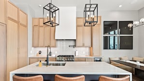 A modern kitchen with wooden cabinets, a central island with bar stools, and pendant lighting.