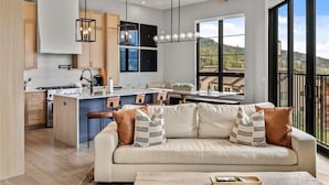 A modern kitchen with a central island, pendant lighting, and a view of the outdoors through large windows.