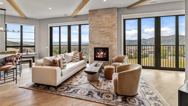 A spacious living room with a stone fireplace, large windows, and a view of the mountains.