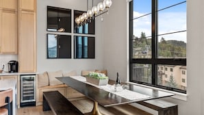 A modern kitchen with a dining area, large windows, and a view of buildings.