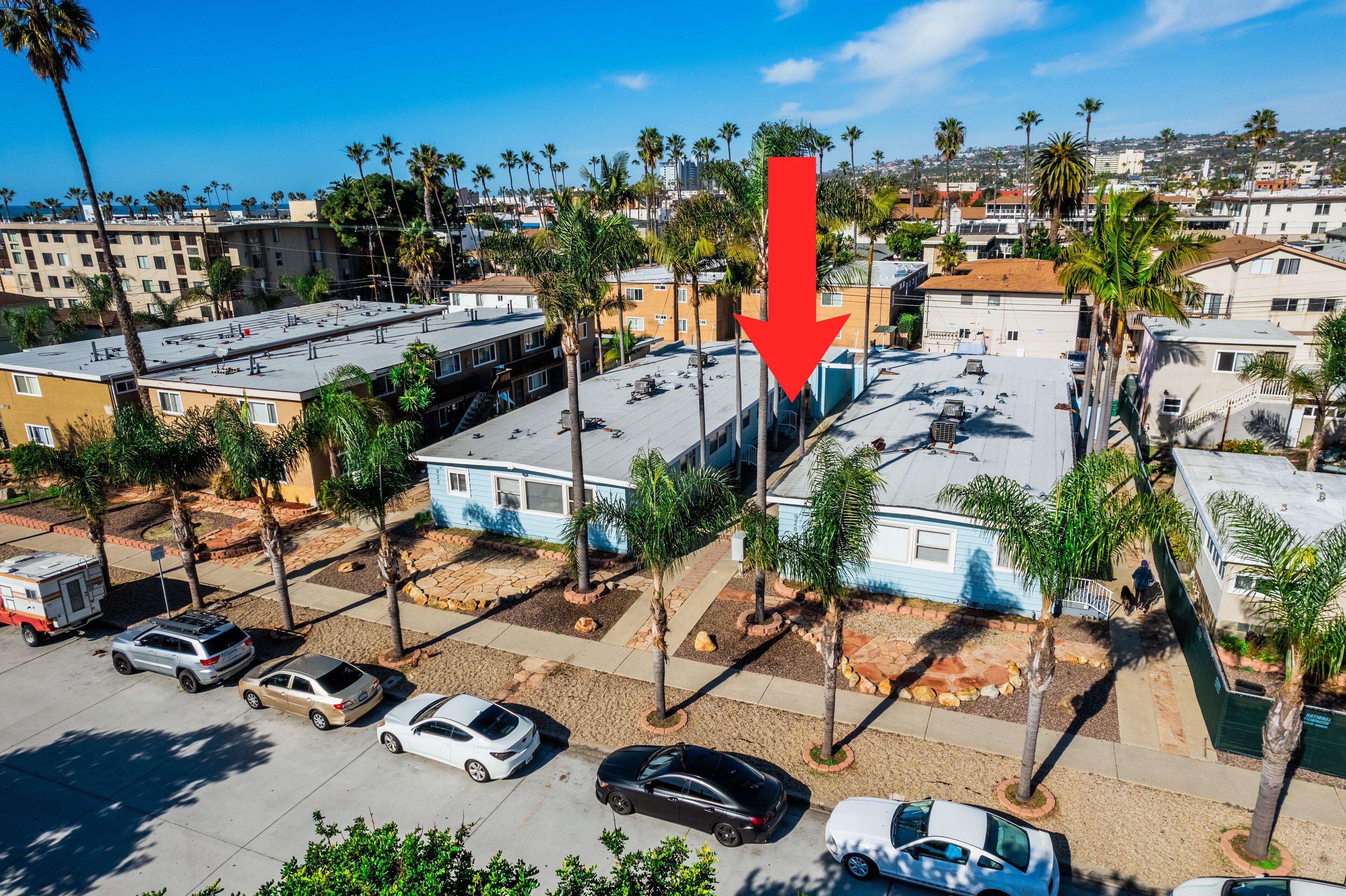 A residential area with multiple two-story houses, palm trees, and parked cars.