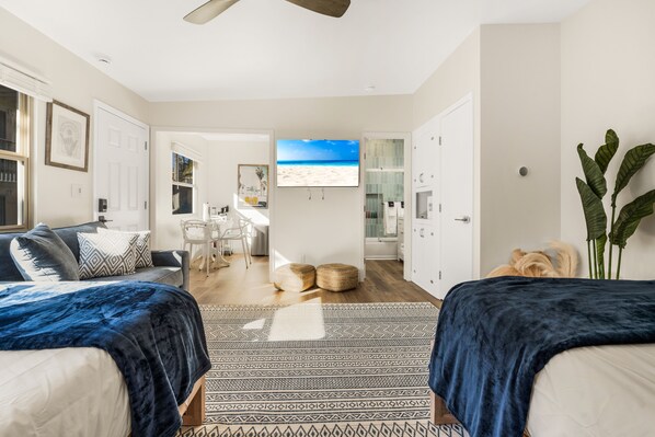 A modern bedroom with two beds, a large TV, and a view of the beach.