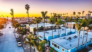Un hotel costero con varios edificios azules, un estacionamiento y palmeras.
