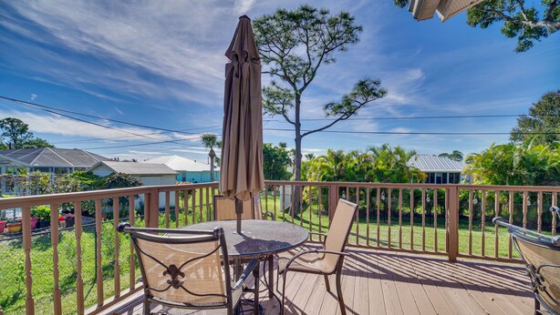Een houten terras met een tafel, stoelen, een parasol en uitzicht op een woonwijk met huizen en bomen.