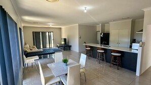 A modern apartment with a dining area, kitchen, and a balcony with curtains. - Quiet Busselton Retreat (West Busselton)
