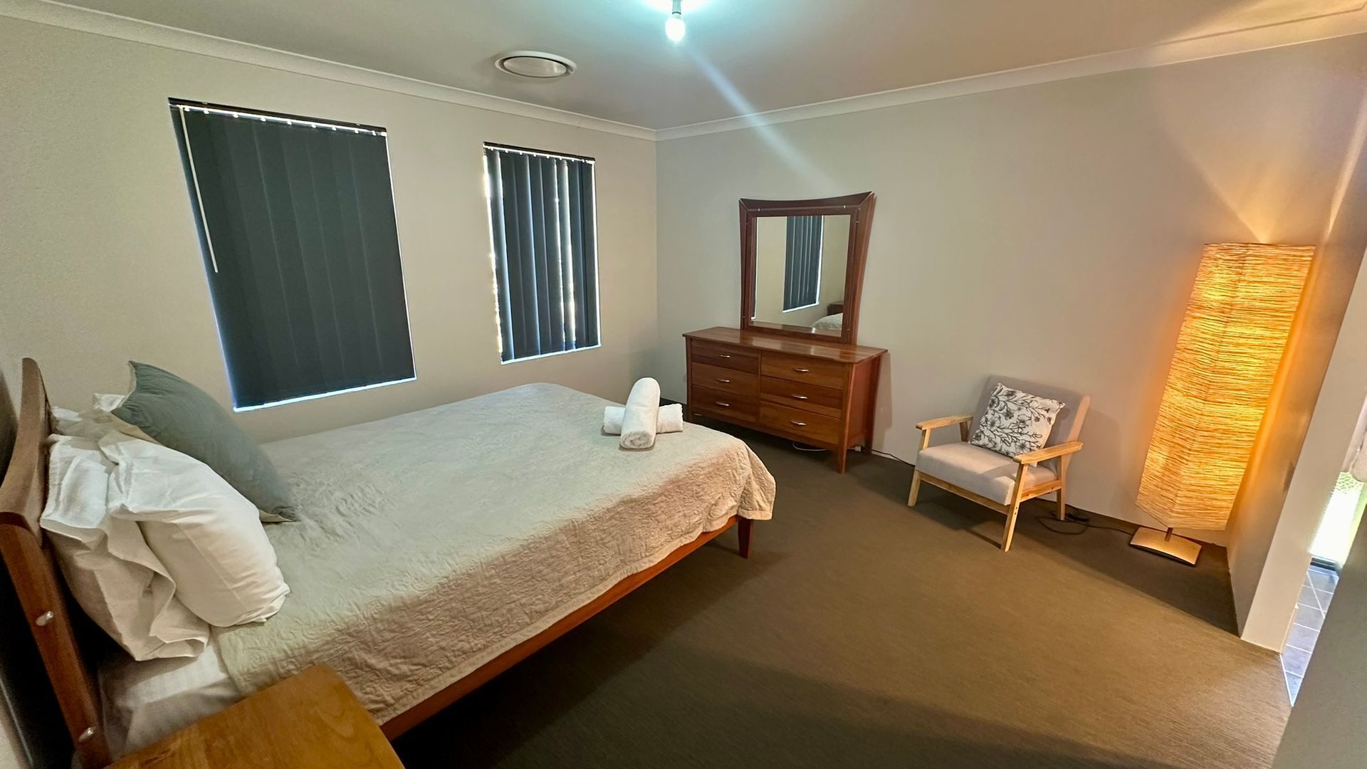 A bedroom with a bed, a dresser, a chair, and a standing lamp.