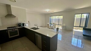A modern kitchen with a central island, stainless steel appliances, and a dining area with a view of the outdoors. - Quiet Busselton Retreat (West Busselton)