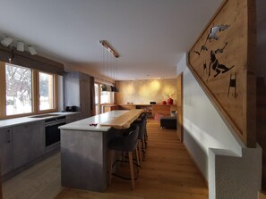 A modern kitchen with a central island, bar stools, and a large window. - Premium Chalet in Tauplitz With Sauna and Pool (Bad Mitterndorf)