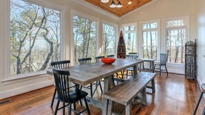 Un coin repas avec une table en bois, des chaises noires et un bol rouge. De grandes fenêtres offrent une vue sur les arbres.