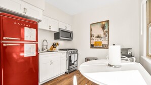 A modern kitchen with white cabinets, a red Galanz refrigerator, a microwave, an oven, and a dining table with chairs.
