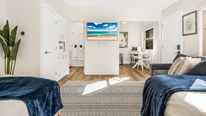 A modern, well-lit room with a large bed, a desk, and a view of the beach through a window.