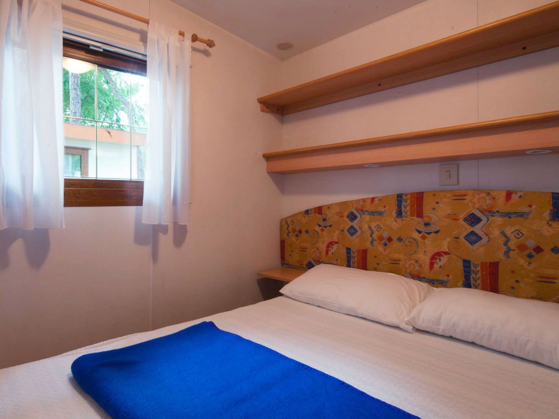 Un dormitorio con cama, ventana con cortinas y cabecera de madera con diseño estampado.