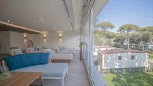 Un intérieur moderne avec une longue rangée de canapés blancs et une table en bois, de grandes fenêtres offrant une vue sur un quartier résidentiel.