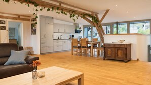 Una cocina moderna con armarios blancos, un comedor con sillas de madera y una sala de estar con un sofá marrón y una mesa de centro.