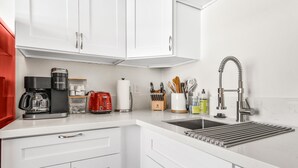 A modern kitchen with white cabinets, a coffee maker, a red toaster, and a stainless steel sink. - Pacific Beach Retreat in Heart of PB - Luxe Studio - Sleeps 5 w/ A/C  (San Diego)
