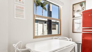 A room with a white table and chairs, a red refrigerator, a window with a view of palm trees, and a door with a number. - Pacific Beach Retreat in Heart of PB - Luxe Studio - Sleeps 5 w/ A/C  (San Diego)