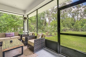 A covered outdoor seating area with wicker furniture, a coffee table, and a view of a grassy yard with trees. - 3 Mi to USF: Dog-Friendly Home w/ Large Yard (Lutz)