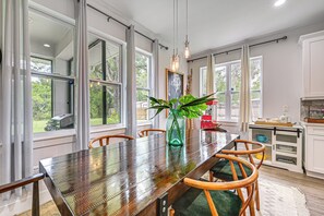 Un coin repas avec une table en bois, des chaises, un vase avec une plante, et un espace cuisine avec des placards et un plan de travail.