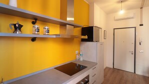 A kitchen with a yellow wall, a stainless steel range hood, a black refrigerator, and a white door. - The Yellow Petal (Verona)