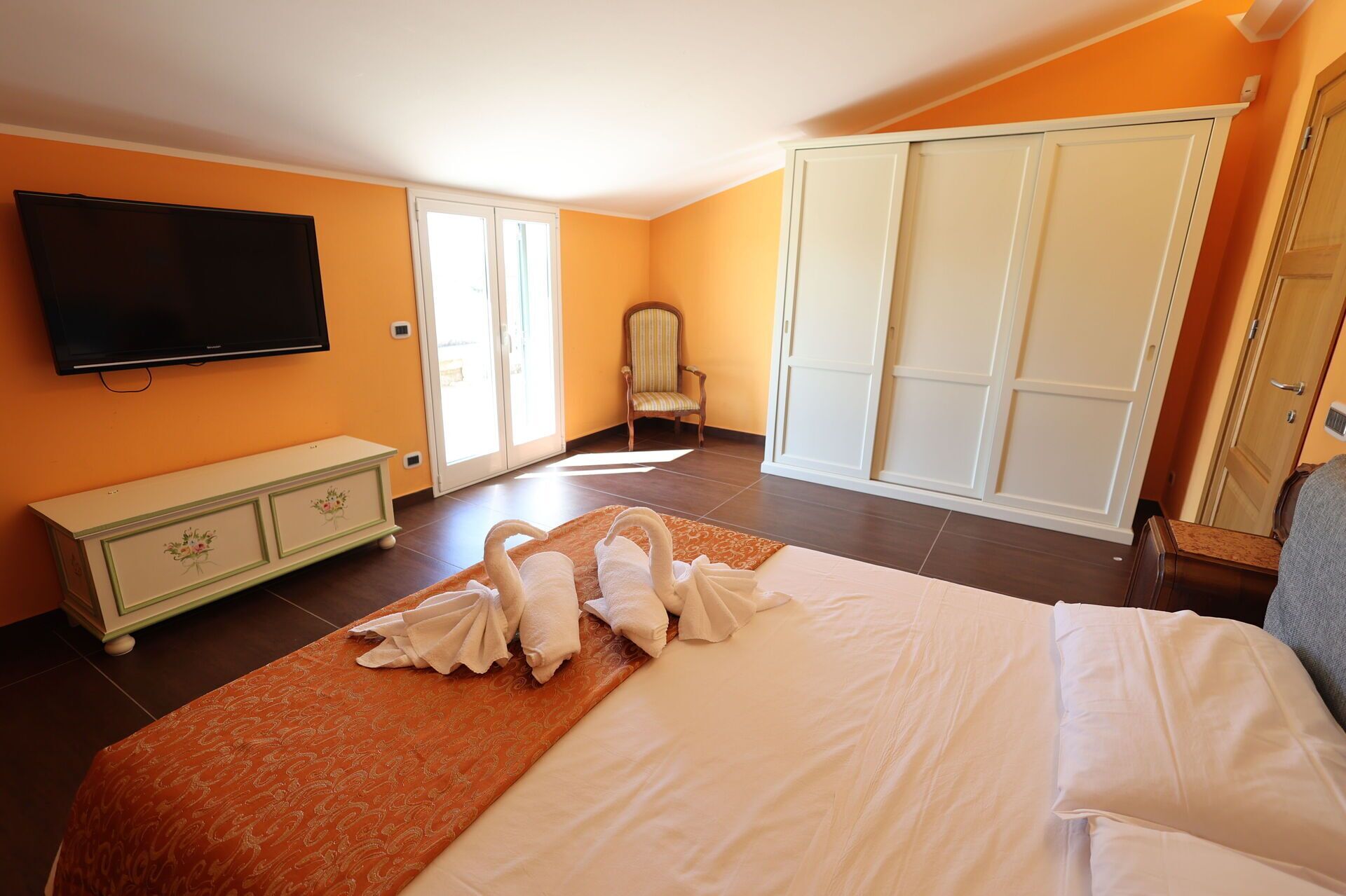 A bedroom with a bed, a TV, a wardrobe, and a chair.