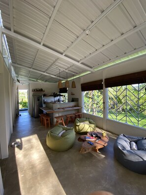 Amplia sala de estar con techo alto, cocina al fondo y grandes ventanales con vistas a zonas verdes.