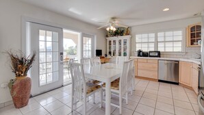 Une cuisine spacieuse avec des meubles blancs, une table à manger avec des chaises et une grande fenêtre qui laisse entrer la lumière naturelle.